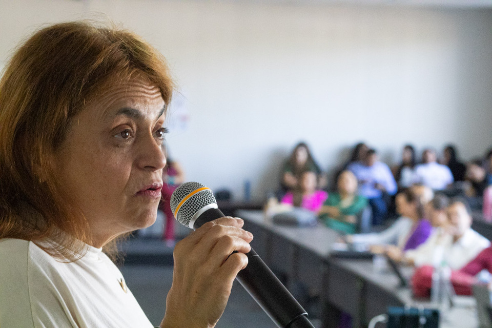 Mulher fala ao microfone diante de uma plateia